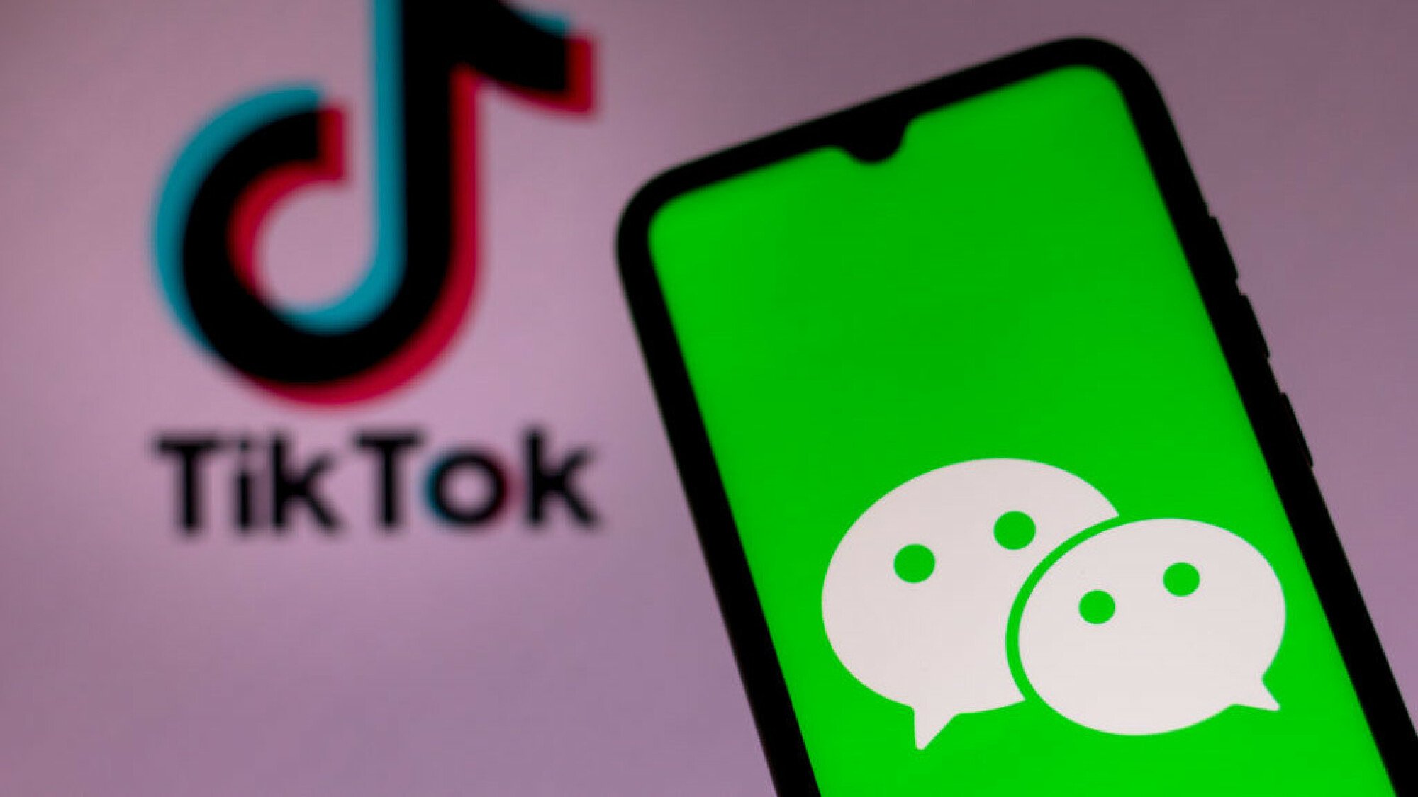 A WeChat logo is seen displayed on a smartphone with a TikTok logo in the background.